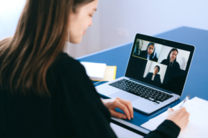 An image of a person taking notes and participating in a virtual meeting on their laptop.