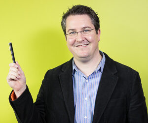 A man smiles at the camera while holding a pen.