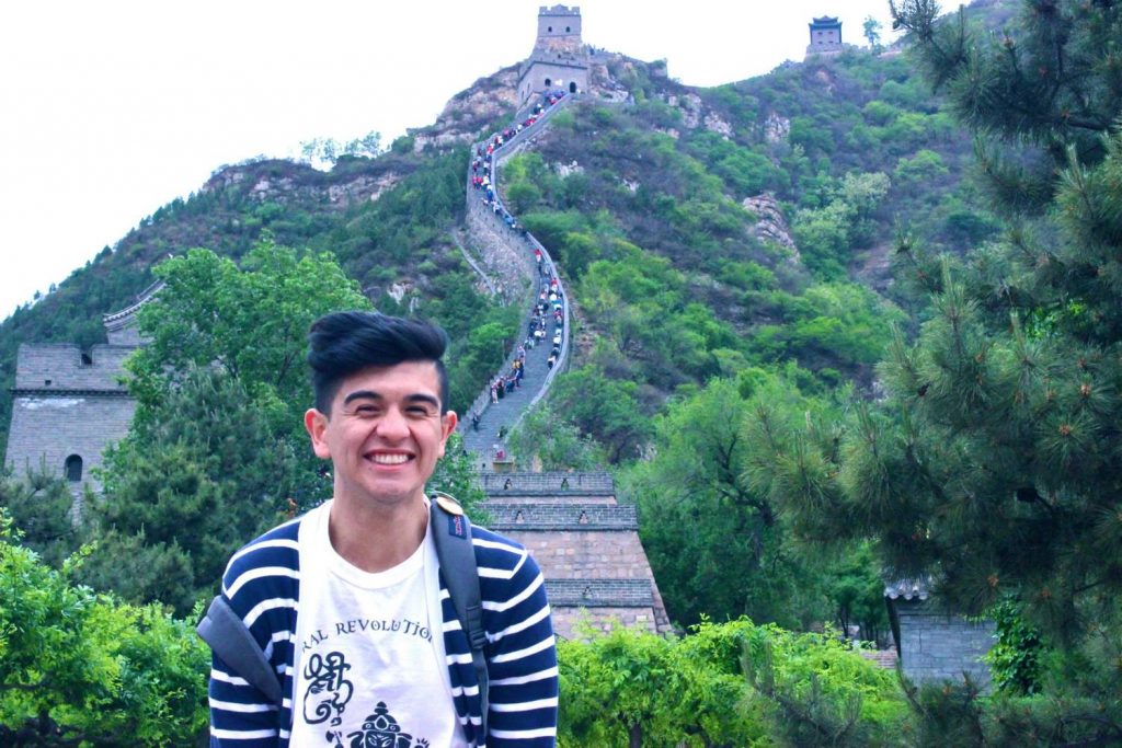 A man smiling in front of the Great Wall of China.