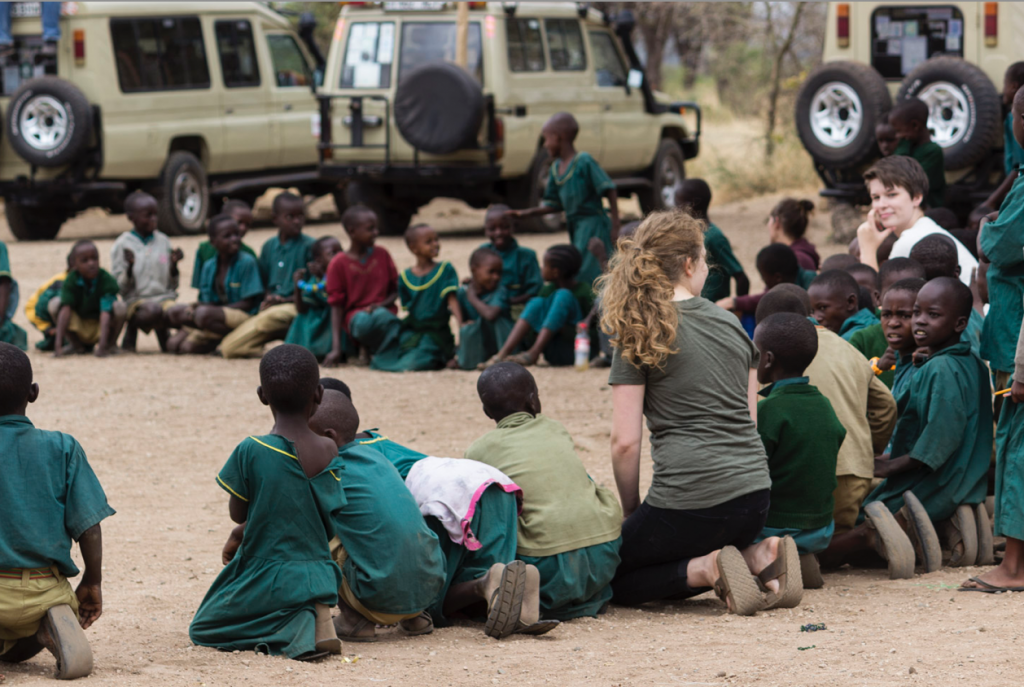 A woman is sitting in a circle with children wearing uniforms.