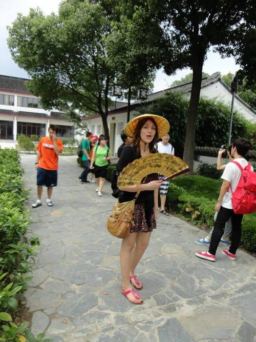 A woman with a traditional Chinese hat and fan is looking at the camera.