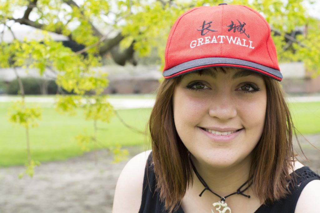 A woman is smiling at the camera while wearing a hat with Chinese letters that reads "Great Wall".