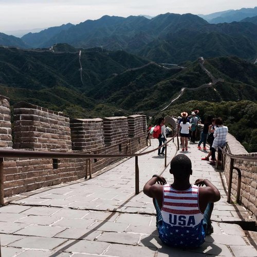 man in USA tank top sitting on the great wall of china
