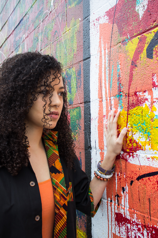 A woman is touching a wall with paint and graffiti on it.