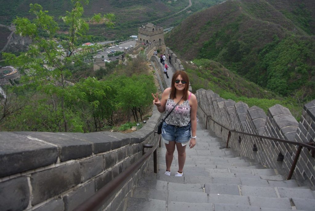 A woman is standing on the Great Wall of China while giving a peace sign.
