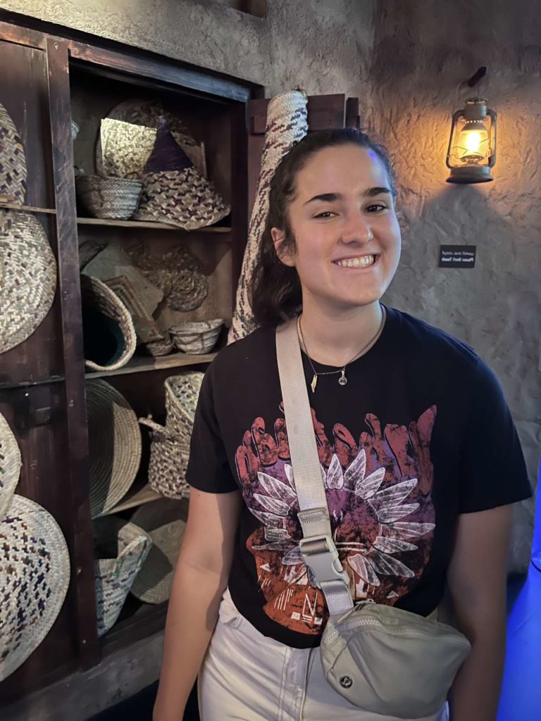 Isabelle Borr, posing with a smile inside of a store of hand-woven baskets and hats.    