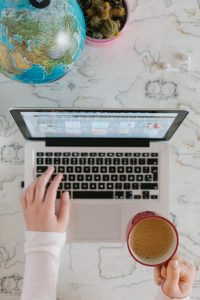 Laptop, coffee, globe, and hand.